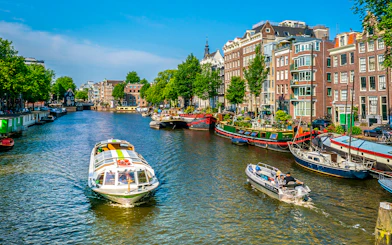 Boats navigating an Amsterdam canal lined with historic buildings and houseboats.