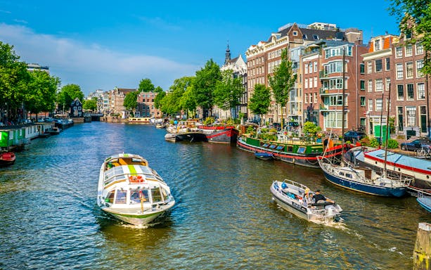 Boats navigating an Amsterdam canal lined with historic buildings and houseboats.