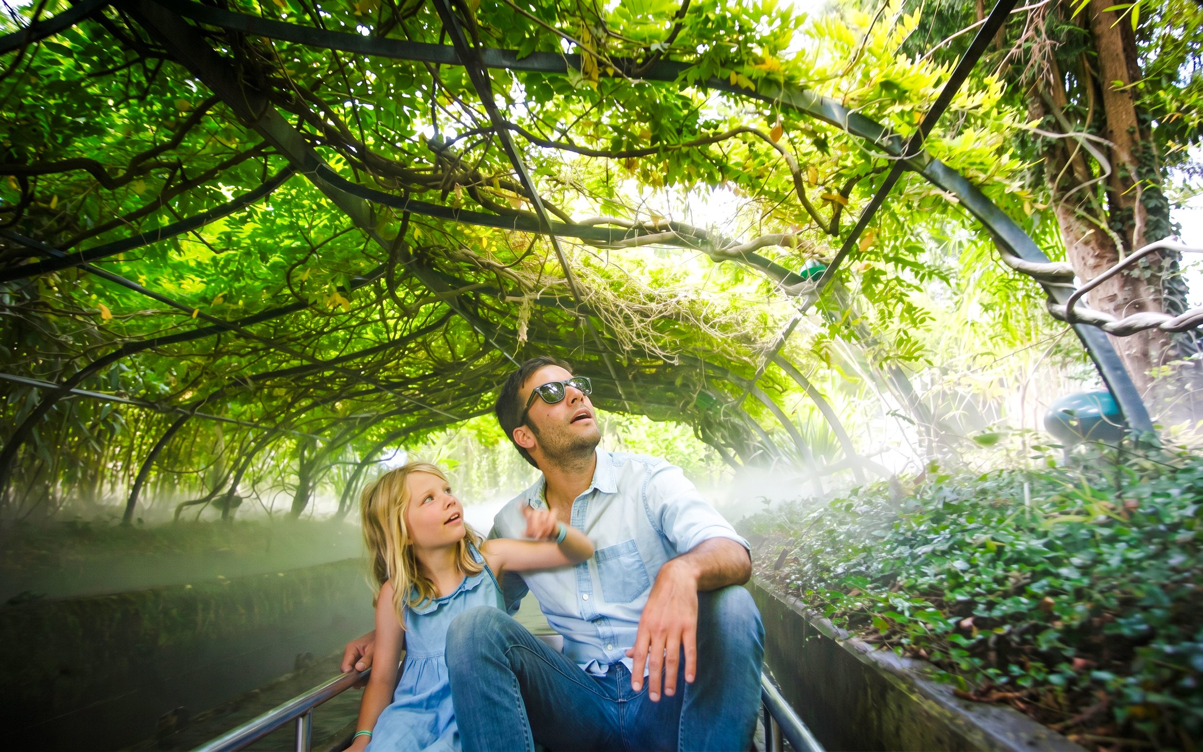 Father and daughter on a boat ride under lush greenery at Jardin d'Acclimatation, Paris.