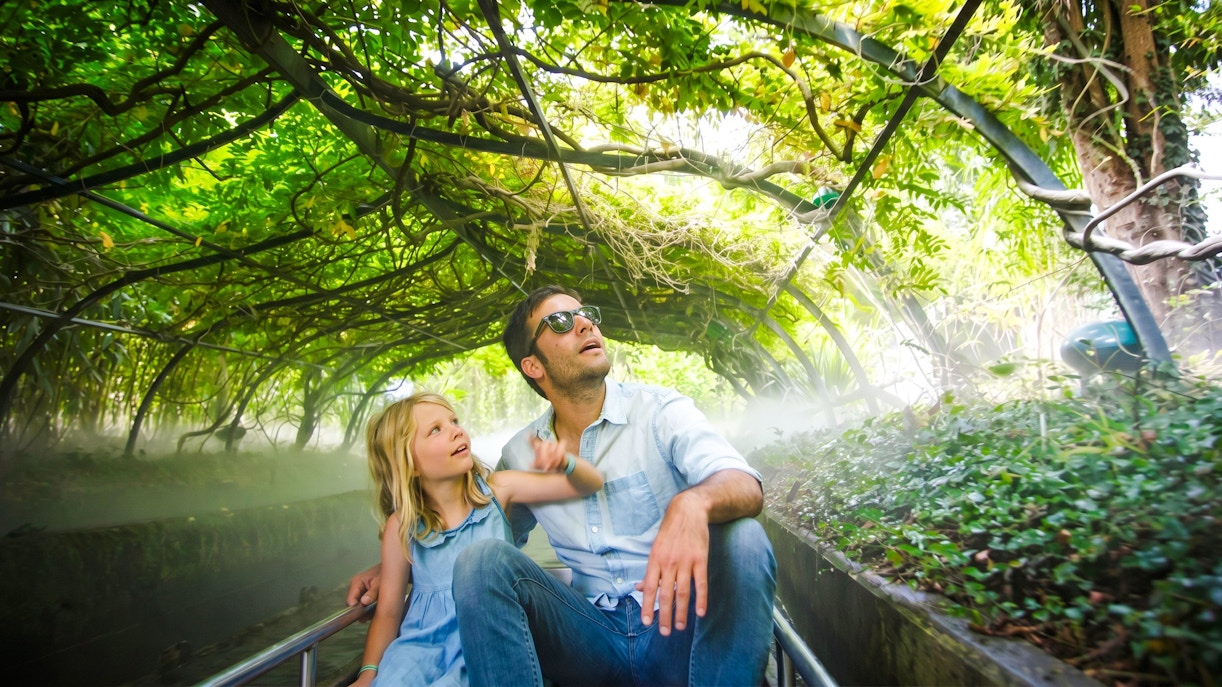 Father and daughter on a boat ride under lush greenery at Jardin d'Acclimatation, Paris.