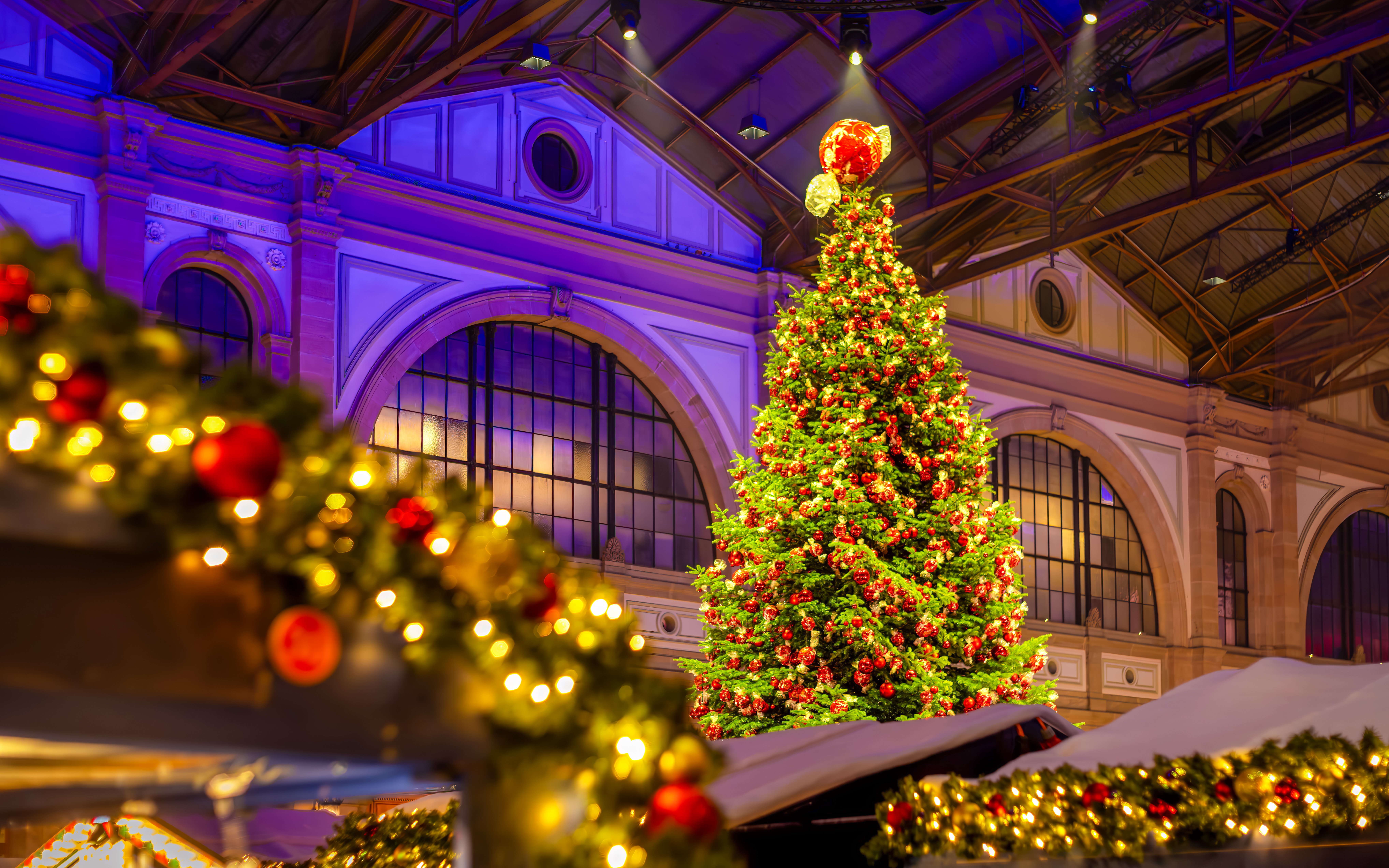 Indoor Christmas market with a large decorated tree and festive lights.