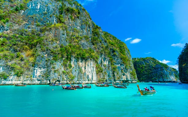 Longtail boats on turquoise waters near limestone cliffs, Phi Phi Islands tour.