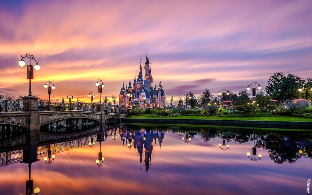 Shanghai Disney castle at sunset with reflections in the water.
