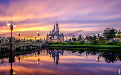 Shanghai Disney castle at sunset with reflections in the water.