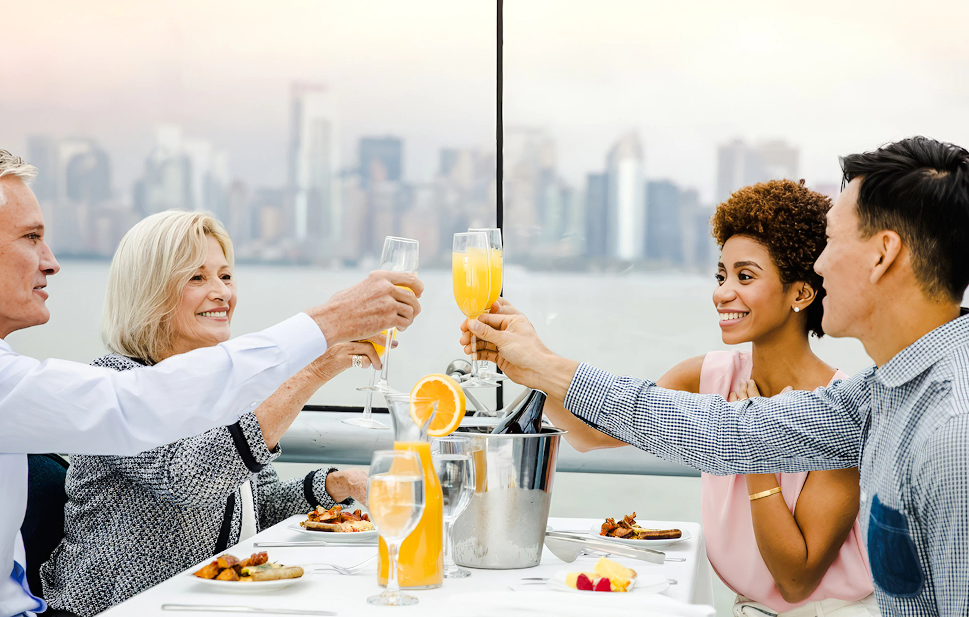 Guests toasting with mimosas on a luxury glass boat brunch cruise by Bateaux, city skyline in background.