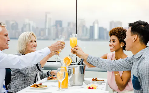 Guests toasting with mimosas on a luxury glass boat brunch cruise by Bateaux, city skyline in background.