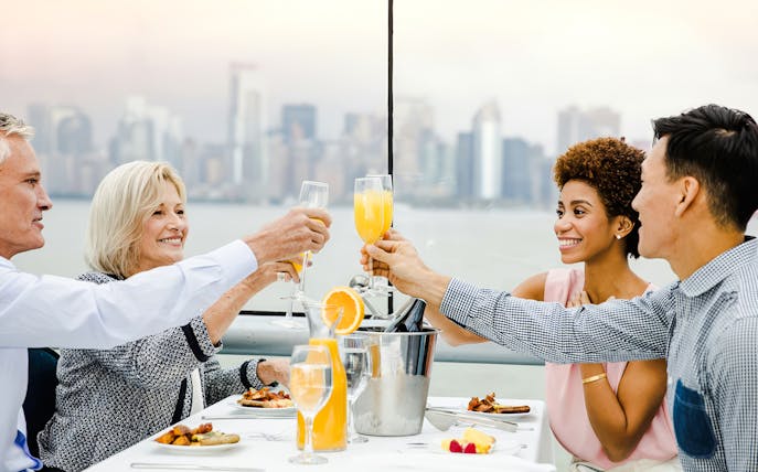 Guests toasting with mimosas on a luxury glass boat brunch cruise by Bateaux, city skyline in background.