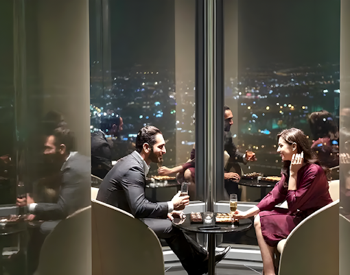 Couple enjoying drinks at Burj Khalifa's At the Top Sky Lounge, overlooking city lights.