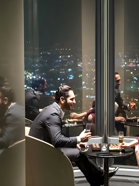 Couple enjoying drinks at Burj Khalifa's At the Top Sky Lounge, overlooking city lights.