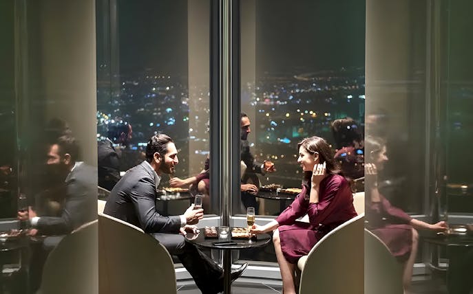 Couple enjoying drinks at Burj Khalifa's At the Top Sky Lounge, overlooking city lights.