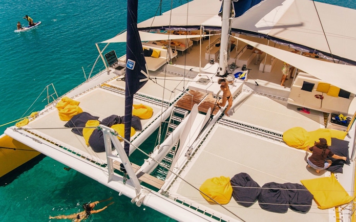 Catamaran deck with people relaxing, paddleboarding, and swimming during Sabre Sunset Cruise.