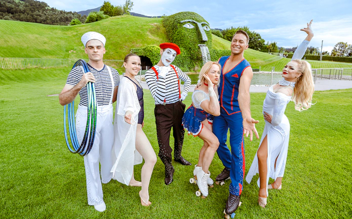 Performers in colorful costumes at Swarovski Crystal Worlds, Innsbruck, with the iconic grass-covered head sculpture.