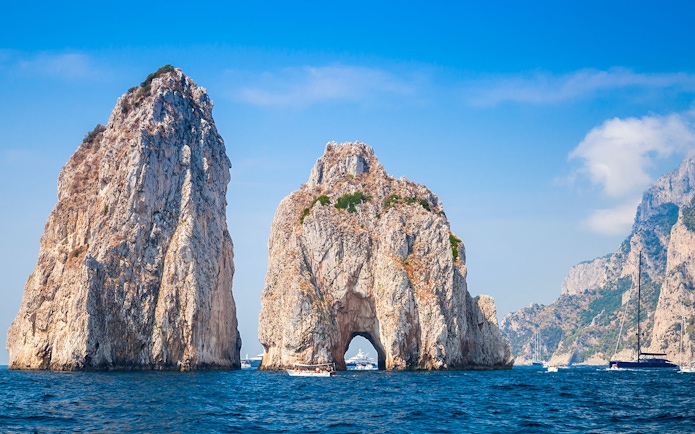 Faraglioni rock formations in Capri with boats in the surrounding blue sea.
