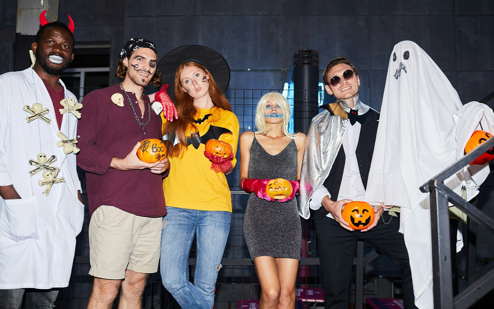 People in Halloween costumes holding pumpkins at a nightclub party.