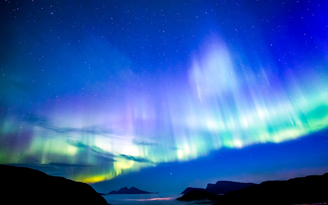 Northern Lights over a coastal landscape viewed from a boat.