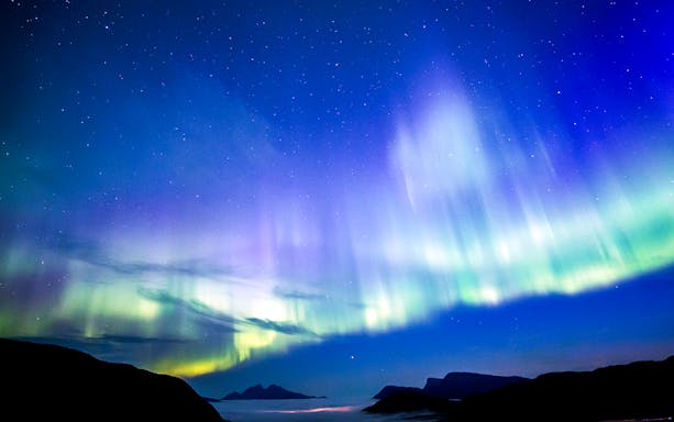 Northern Lights over a coastal landscape viewed from a boat.
