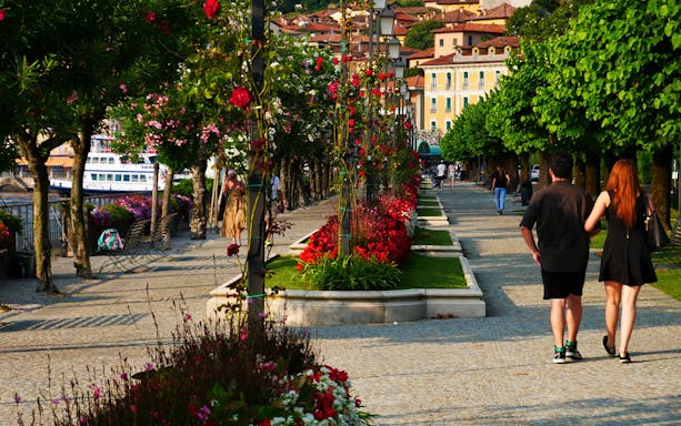 Couple walking along a flower-lined promenade in Bellagio, Lake Como.