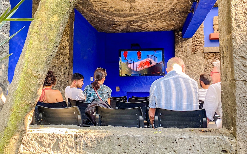 Visitors watching a video at the Frida Kahlo Museum's outdoor area.