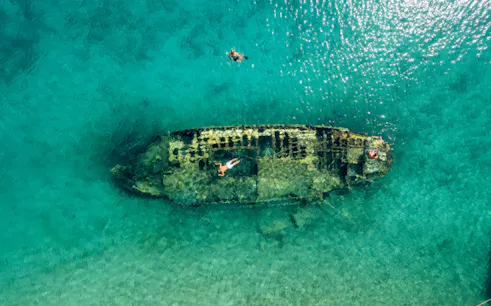 Shipwreck in clear waters near Split, Croatia, with snorkelers exploring.