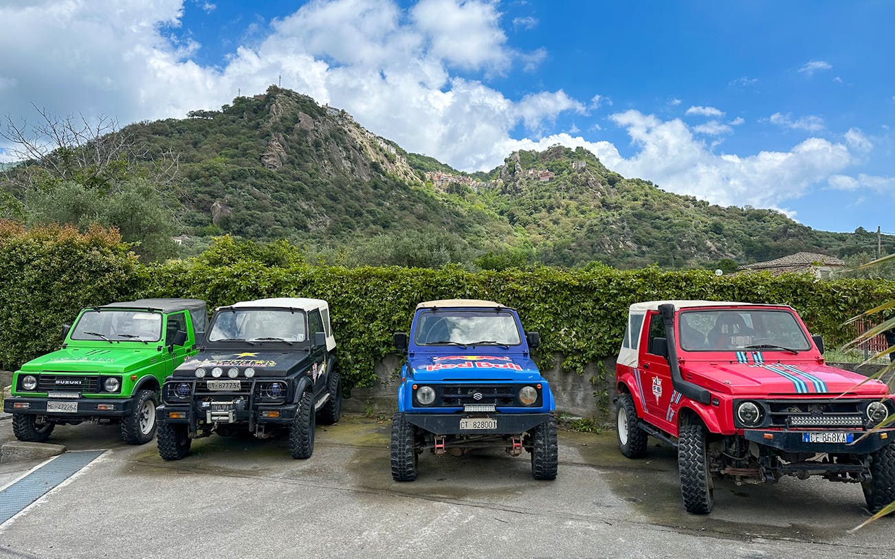 Four colorful 4x4 vehicles parked with Valle Alcantara mountains in the background.