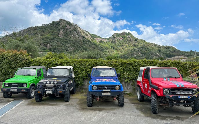 Four colorful 4x4 vehicles parked with Valle Alcantara mountains in the background.