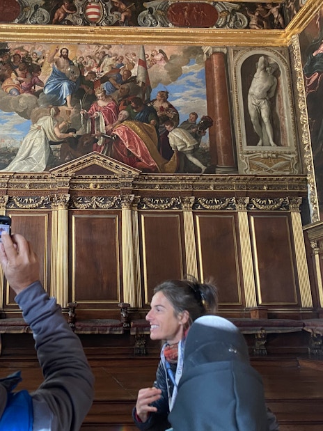 Tour group inside Doge's Palace viewing ornate frescoes and wood paneling.