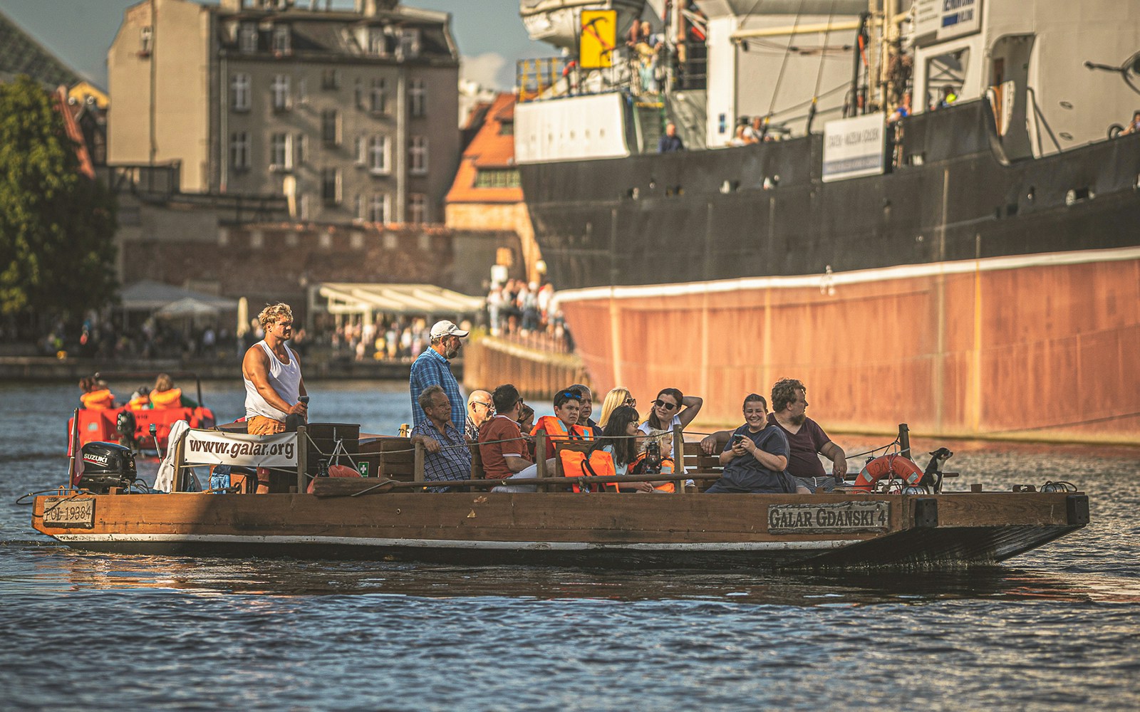 Tourists enjoying a Galar cruise on the Motława River in Gdansk, passing historic buildings.