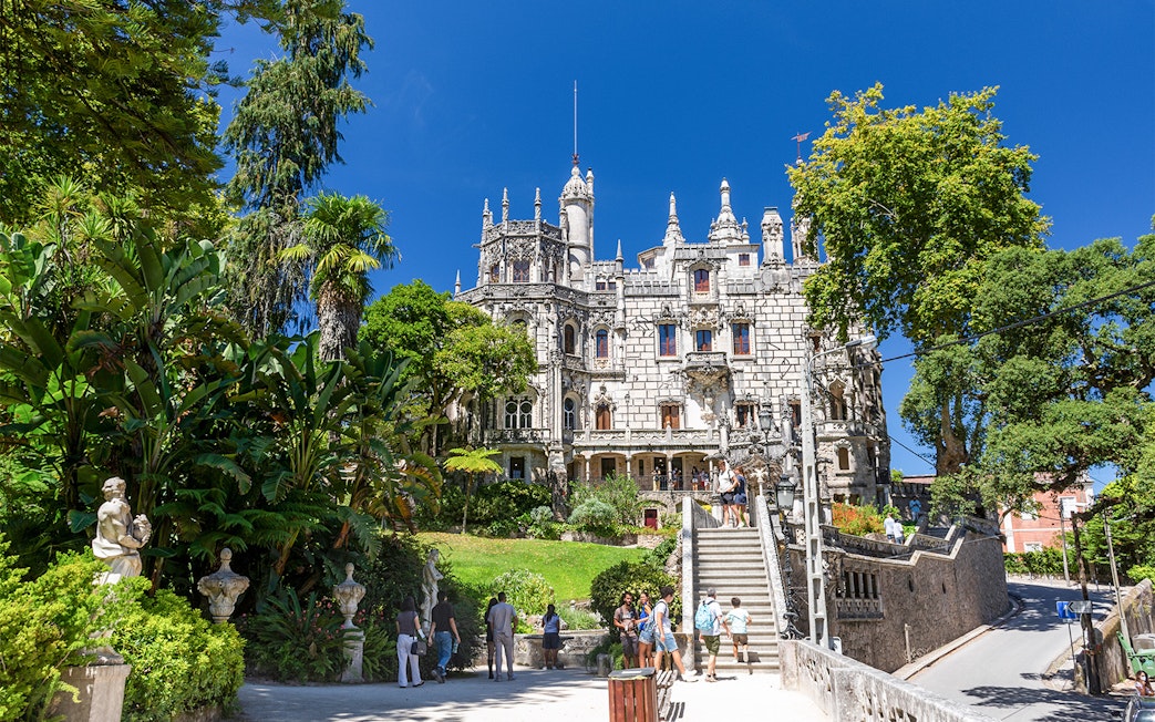 Quinta da Regaleira palace with tourists exploring the gardens and ornate architecture in Sintra, Portugal.