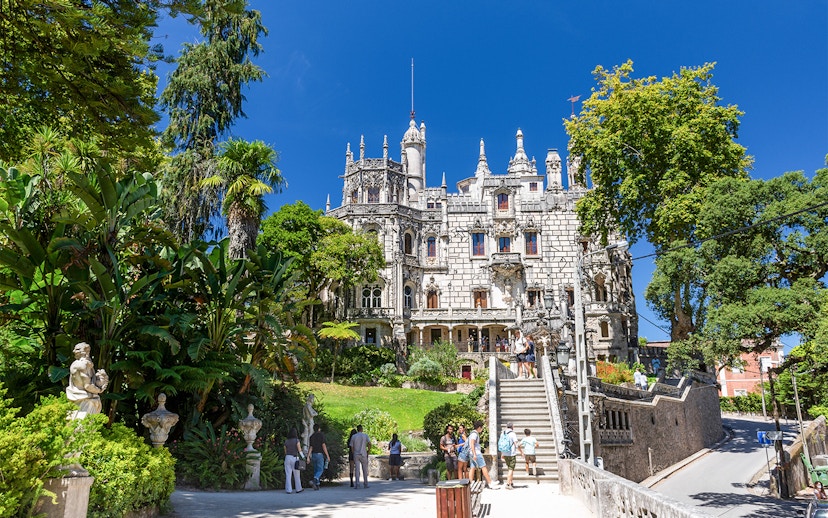 Quinta da Regaleira palace with tourists exploring the gardens and ornate architecture in Sintra, Portugal.