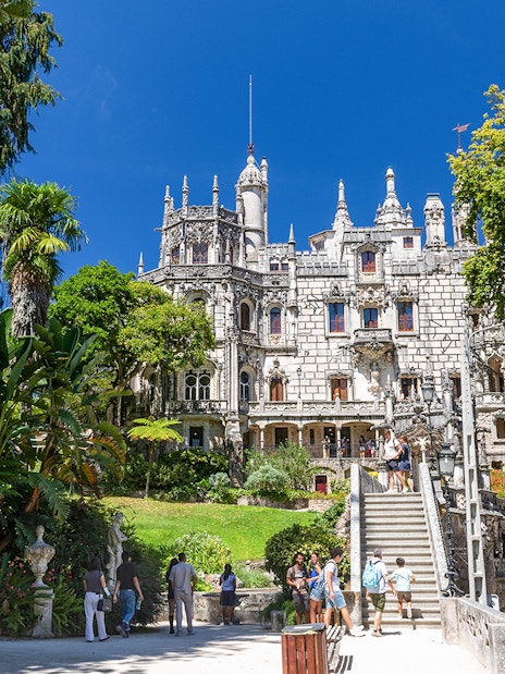 Quinta da Regaleira palace with tourists exploring the gardens and ornate architecture in Sintra, Portugal.
