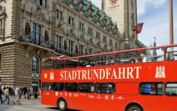 Red double-decker bus in front of Hamburg City Hall during sightseeing tour.