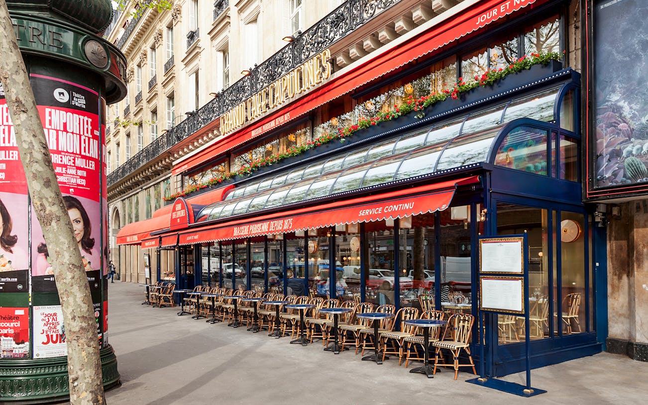 Outdoor seating at Grand Café Capucines, Paris, with red awnings and floral decorations.