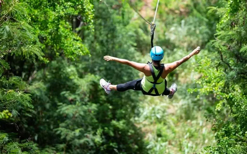 Person ziplining through lush forest in Oahu, part of Off-Road ATV and 3-Zipline Adventure Package.