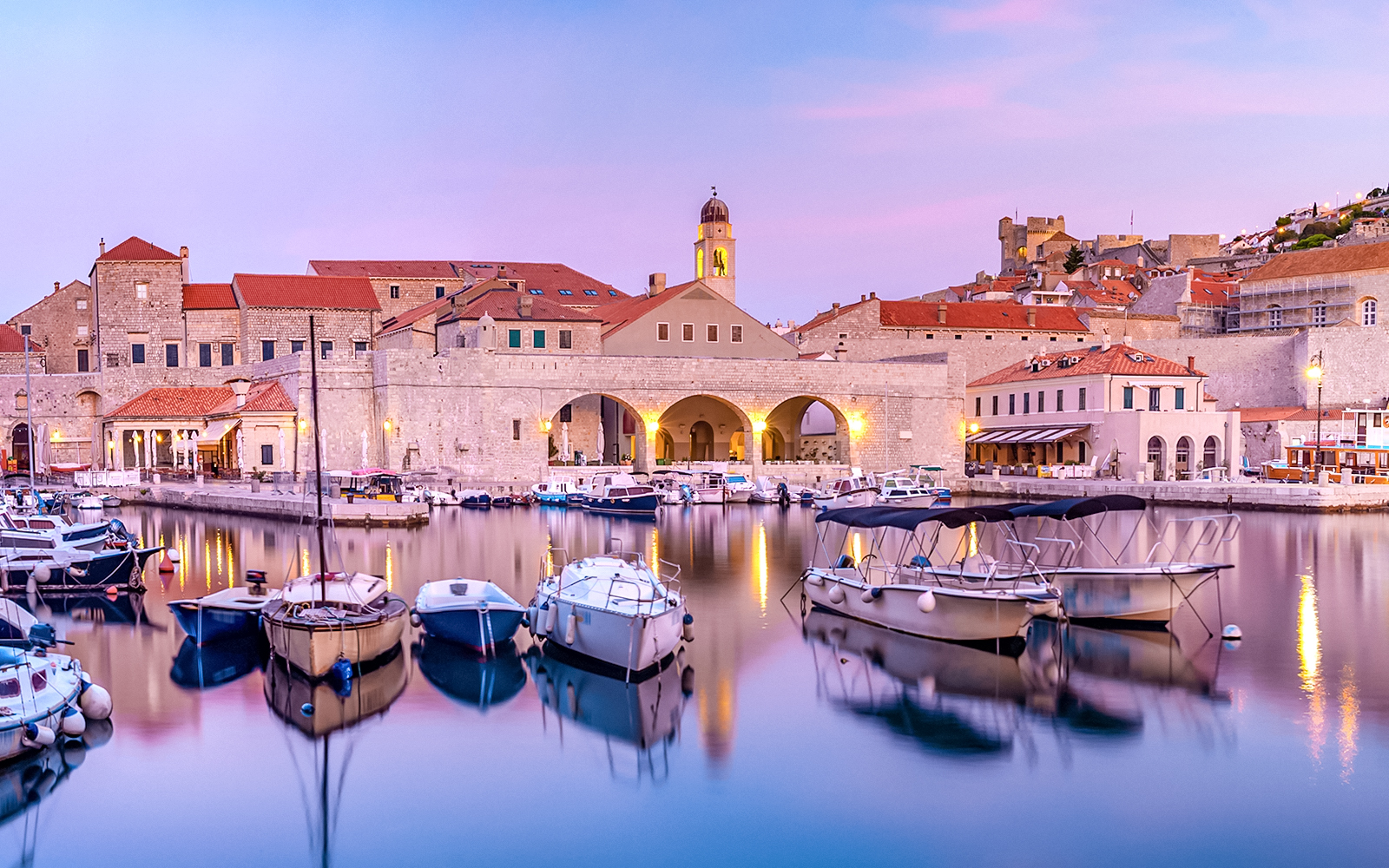 Dubrovnik old town harbor at sunset with boats and historic buildings.