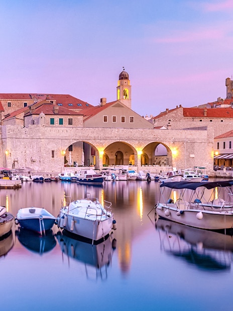 Dubrovnik old town harbor at sunset with boats and historic buildings.