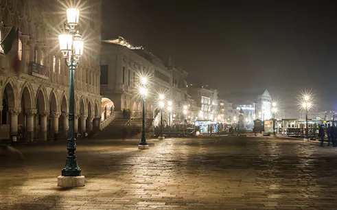 Venice street at night with illuminated lampposts and historic buildings, part of ghost tour.