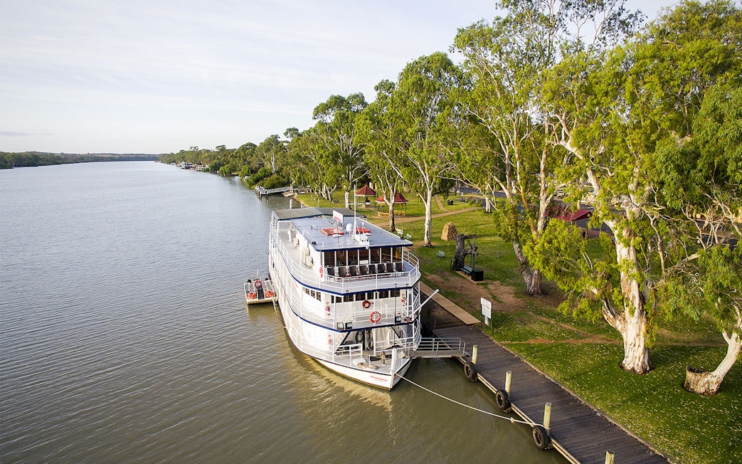 Riverboat docked along the Murray River with lush trees and a wooden pier.