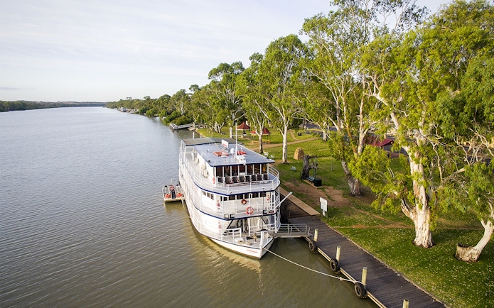 Riverboat docked along the Murray River with lush trees and a wooden pier.