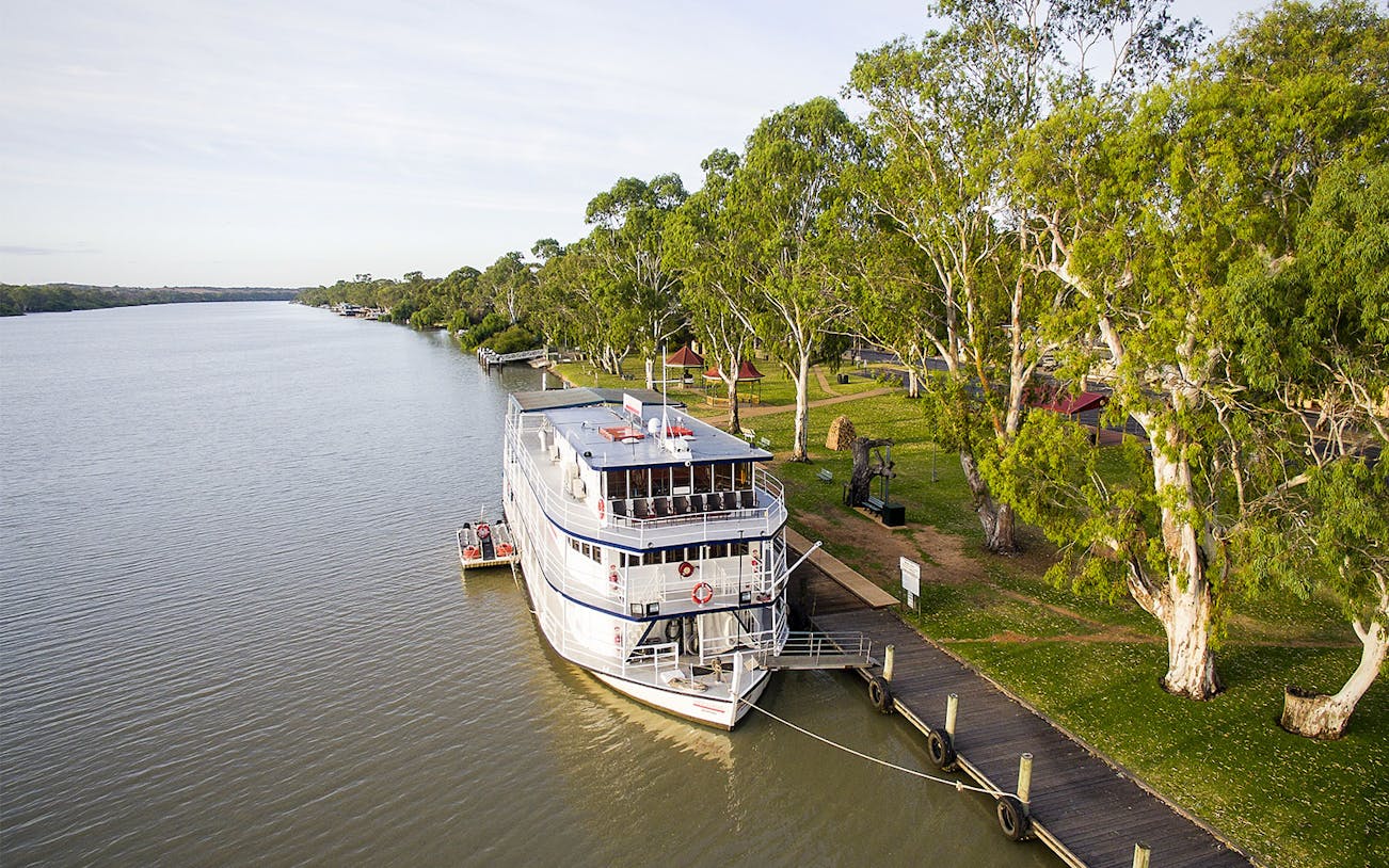 Riverboat docked along the Murray River with lush trees and a wooden pier.
