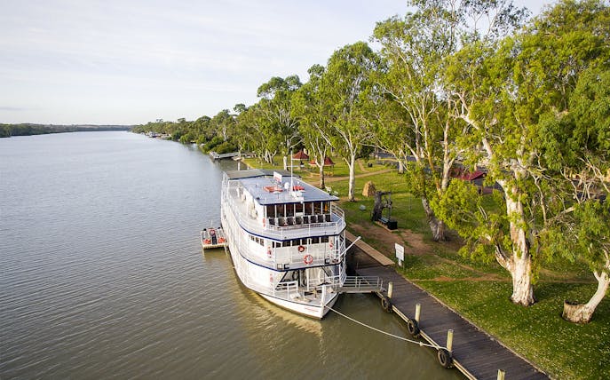 Riverboat docked along the Murray River with lush trees and a wooden pier.