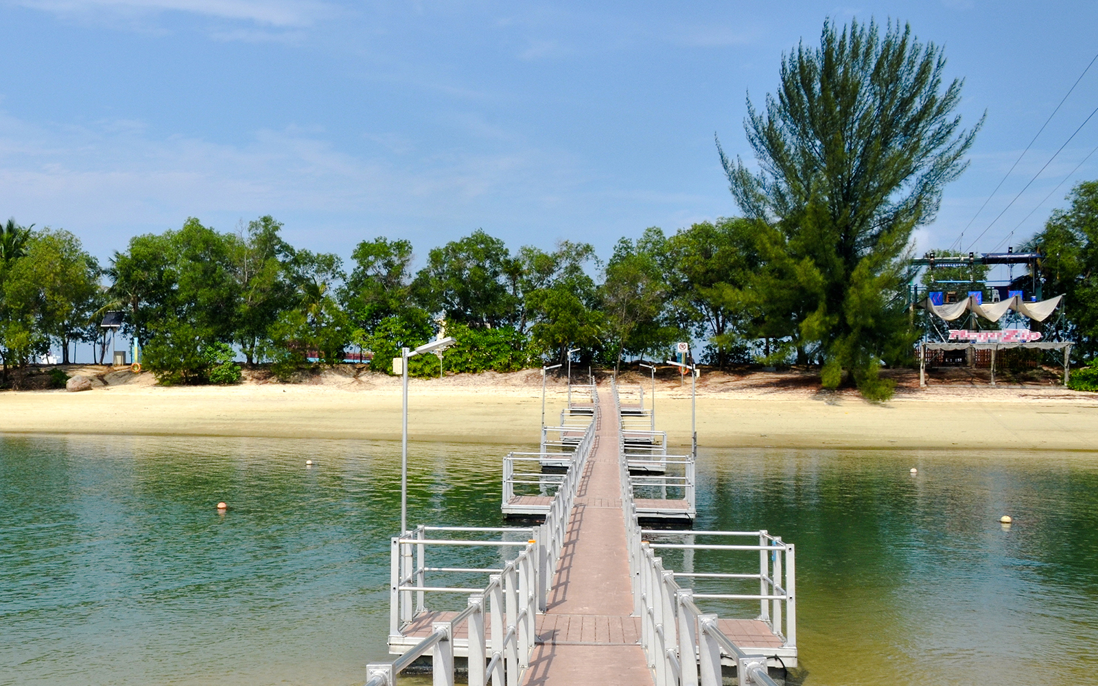 Walkway leading to Tanjong Beach on Sentosa Island, Singapore, with trees and sandy shore.