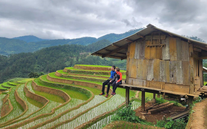 Couple sitting by a wooden hut overlooking rice terraces in Mu Cang Chai, Vietnam.