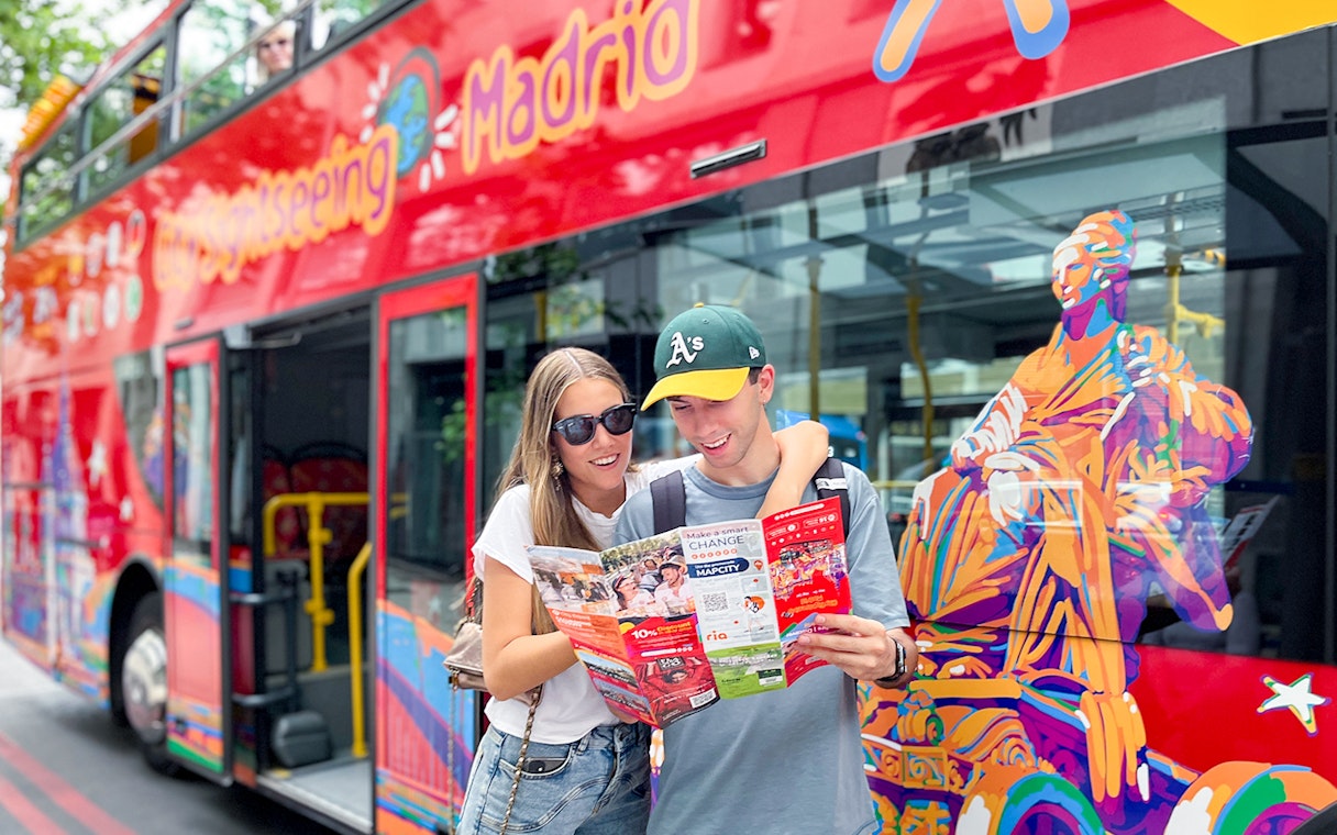 Two people reading a city map near a red double-decker bus in Madrid.