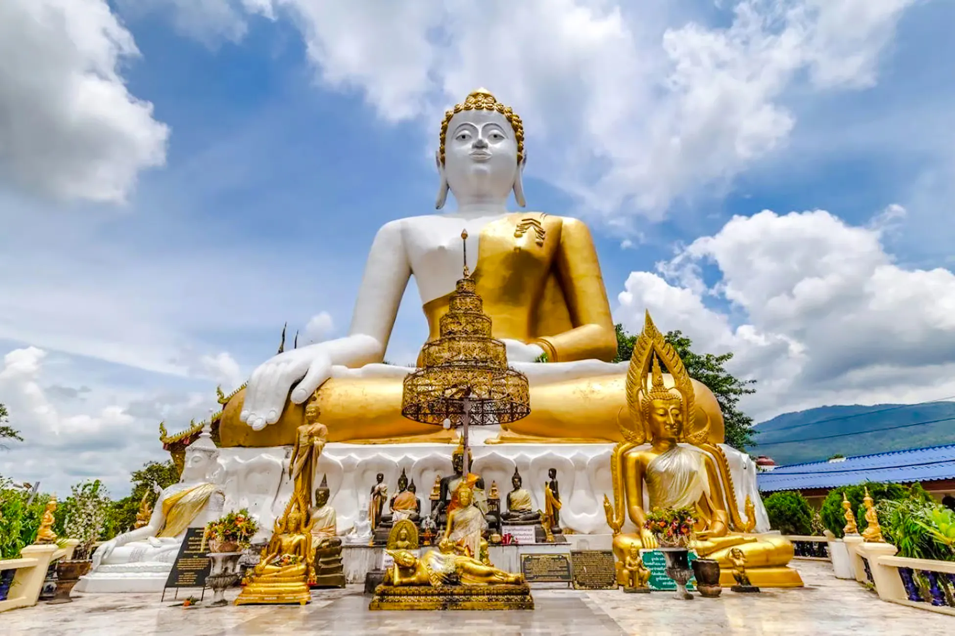 Seated Buddha statue at a temple in Chiang Mai, surrounded by smaller statues and greenery.