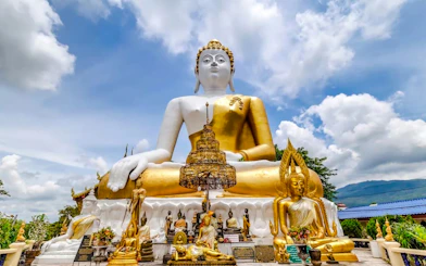 Seated Buddha statue at a temple in Chiang Mai, surrounded by smaller statues and greenery.