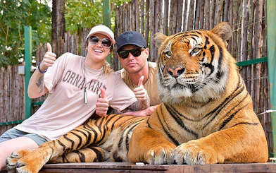 Couple gives thumbs up behind a tiger at Tiger Kingdom experience.
