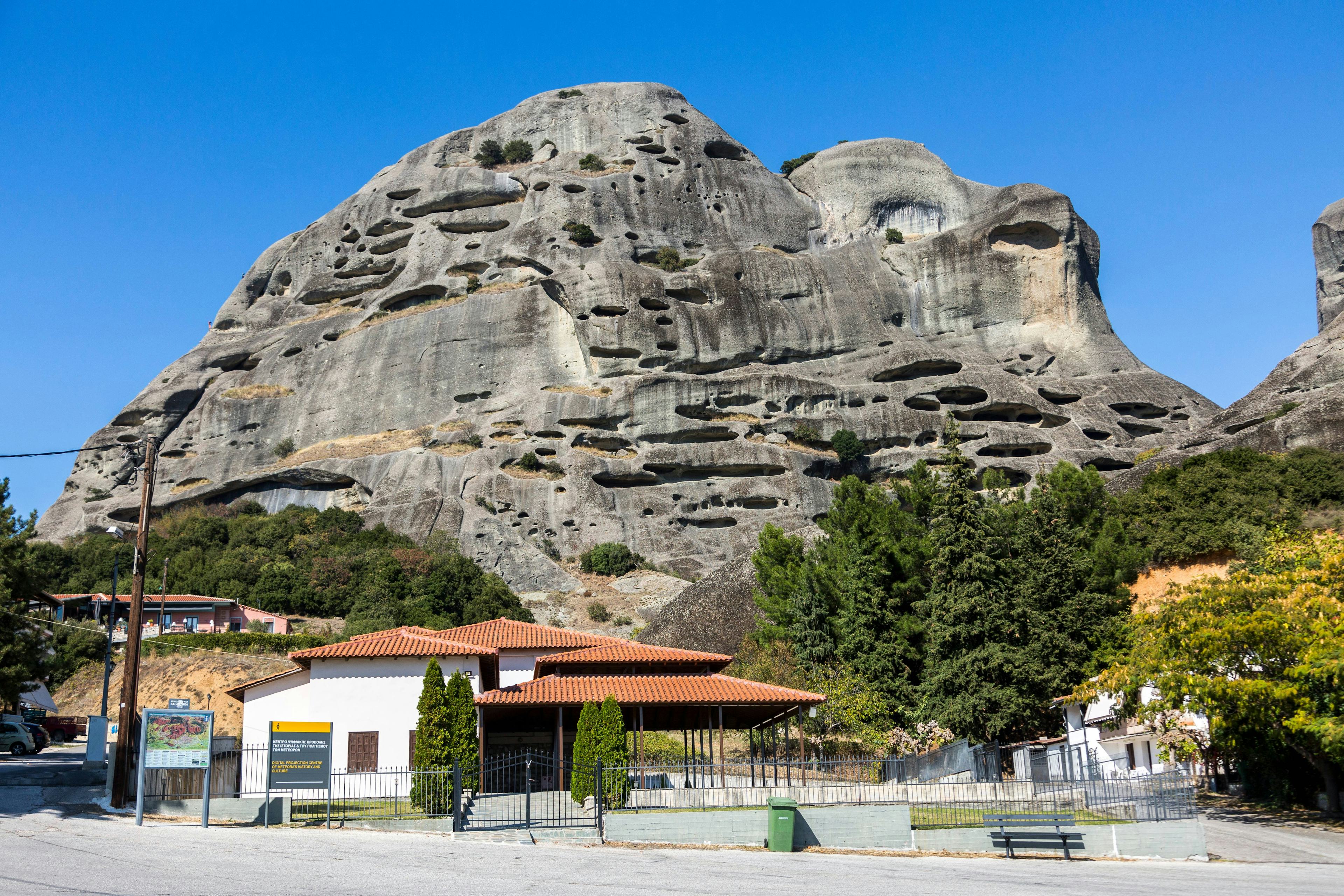 Meteora rock formations with caves and nearby buildings in Greece.