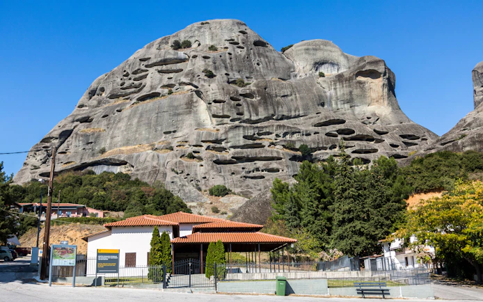 Meteora rock formations with caves and nearby buildings in Greece.
