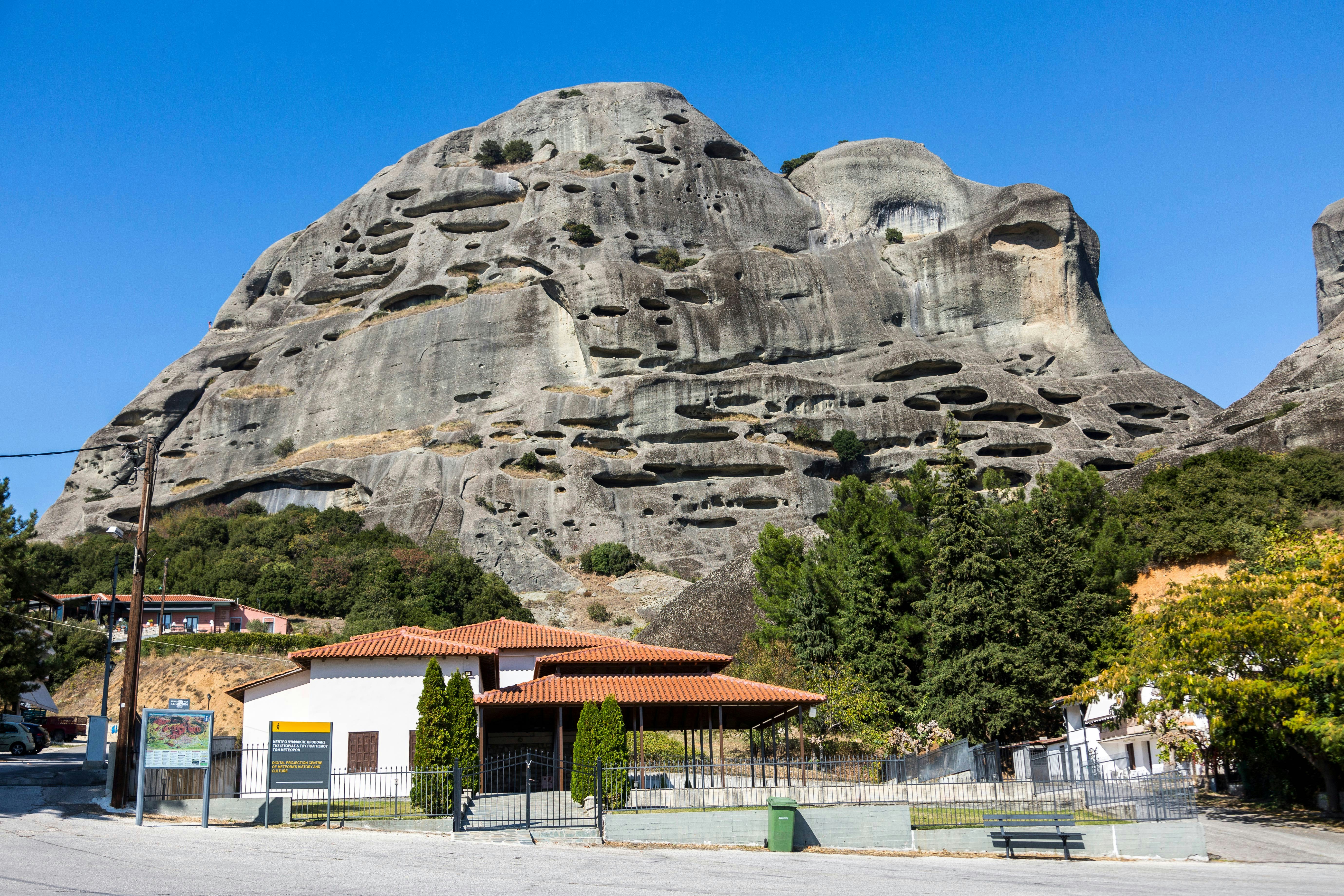 Meteora rock formations with caves and nearby buildings in Greece.