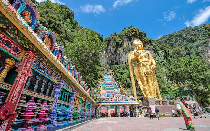 Batu Caves entrance with colorful steps and large golden statue in Kuala Lumpur.